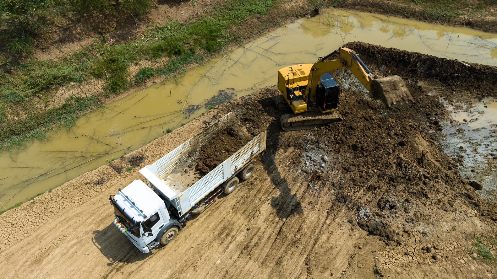 excavating soil into a dump truck to build a pond for store water for use in the dry season for agriculture, aerial top view